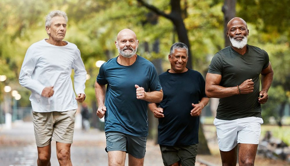 Quatro senhores correndo juntos em um parque arborizado